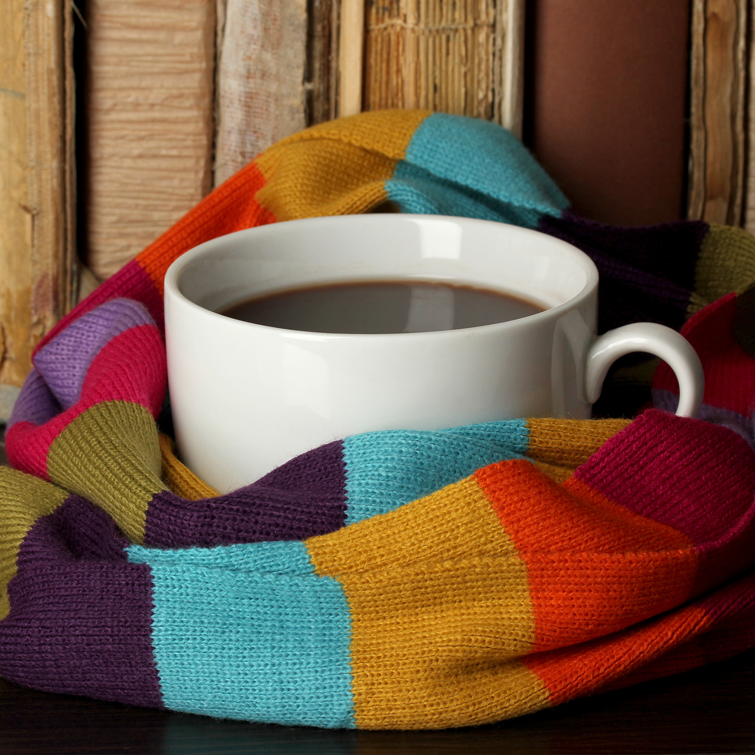 Cup of coffee wrapped in scarf on books background