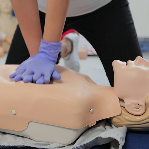 Woman demonstrating CPR on mannequin in first aid class.