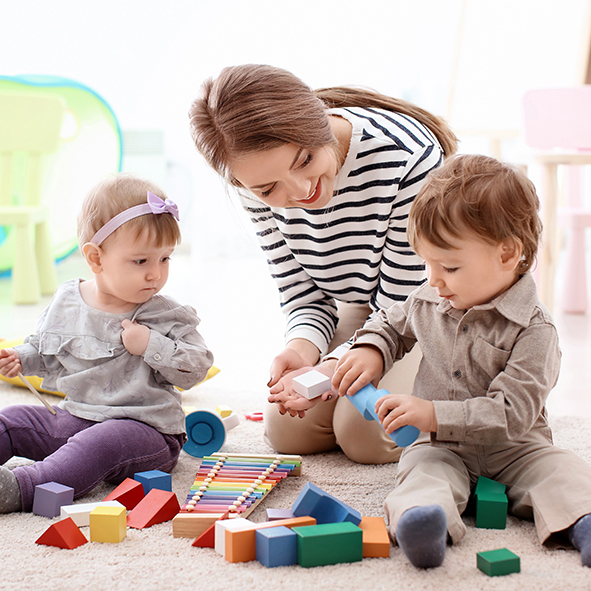 Woman babysitting two toddlers who are playing with blocks