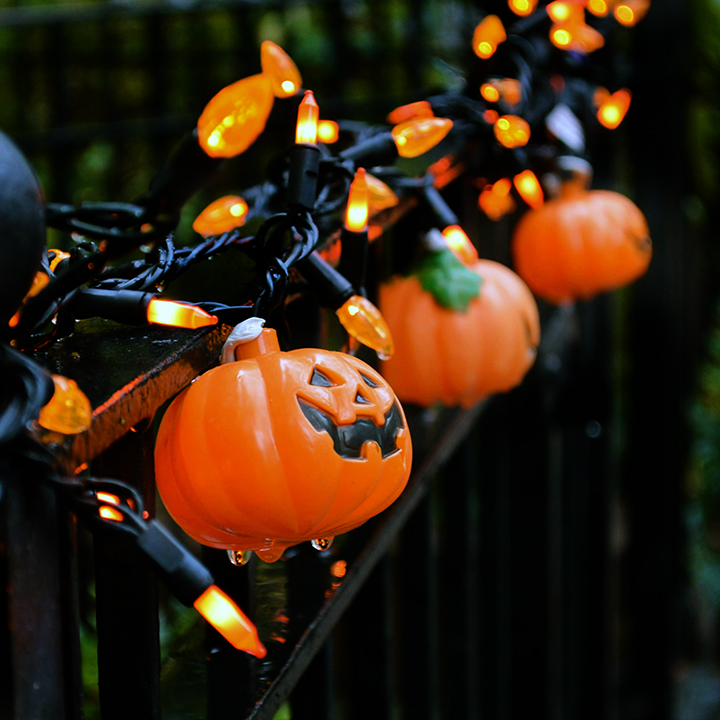 Plastic pumpkin and orange lights on a metal fence in the dark