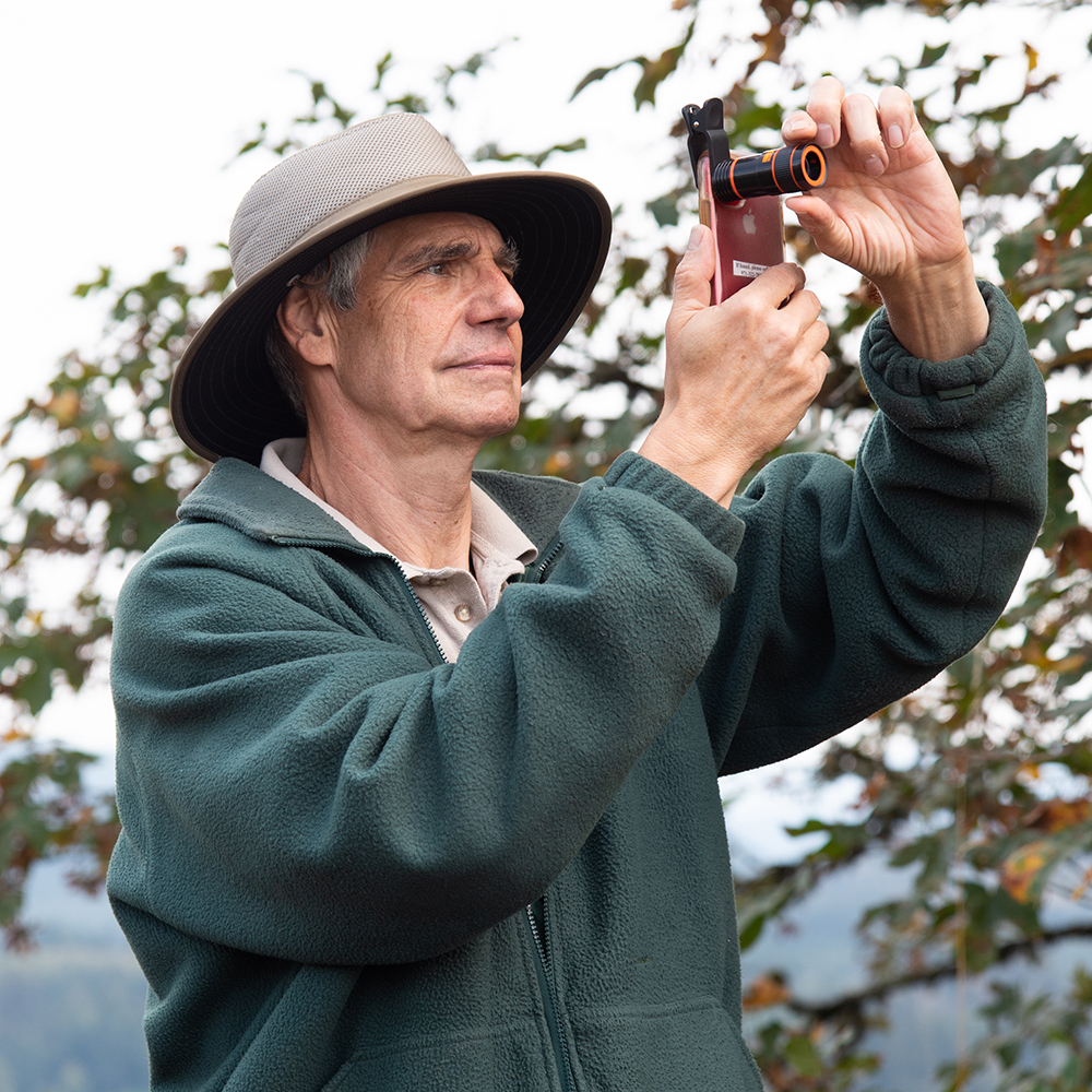 Older man using his phone and a camera lens amplifier to take photos of nature