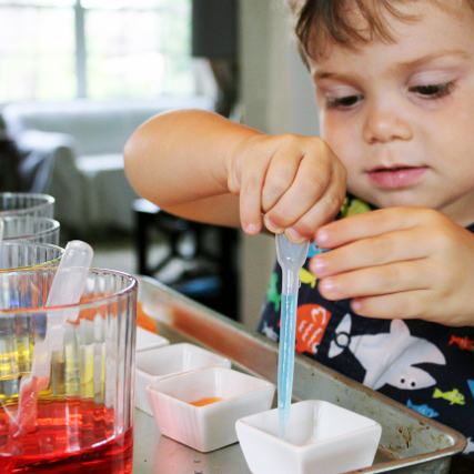 Small kid mixing colors with a dropper in small cups