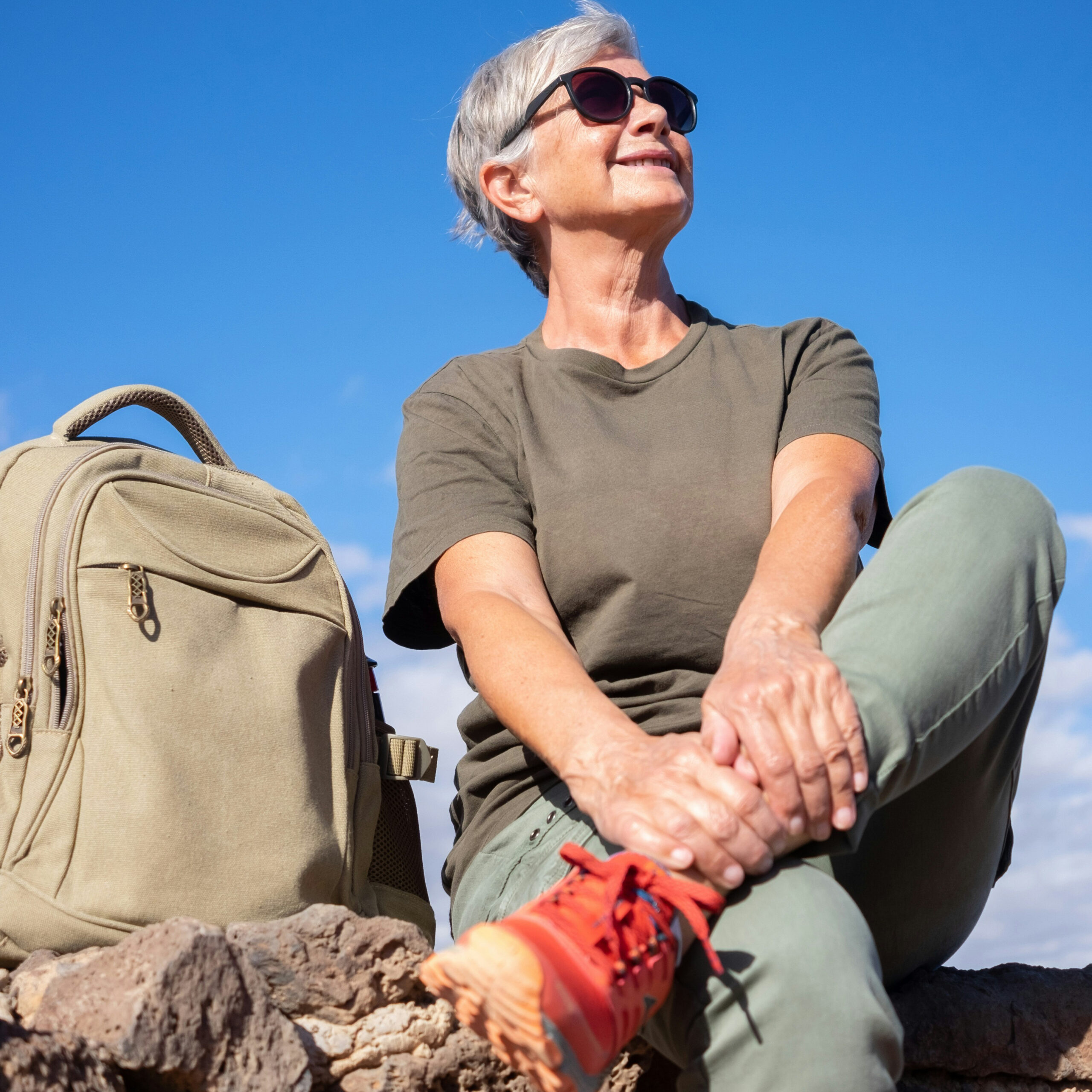 Older woman taking a hiking break on a rock with a backpack beside her