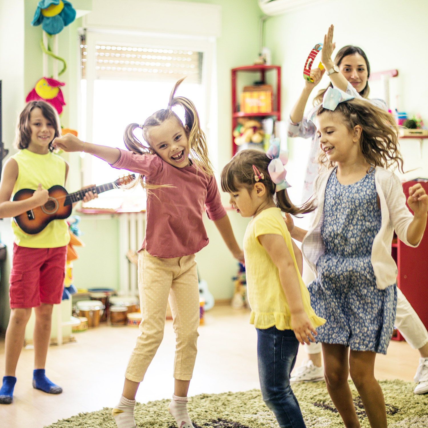 Kids dancing in a room with a teacher playing a tambourine